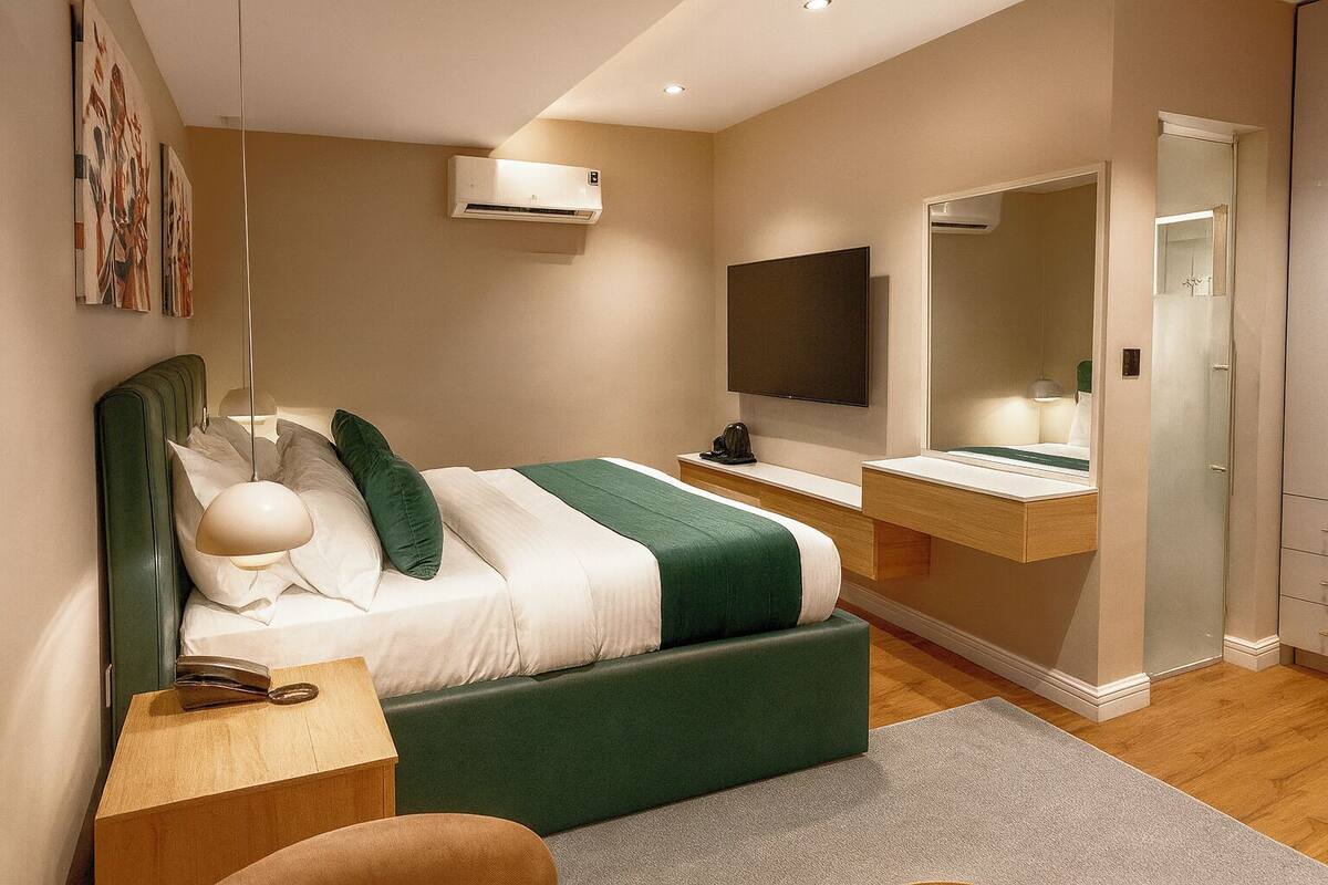 A modern bedroom with a bed, bedside table, TV, mirror, and built-in wardrobe.