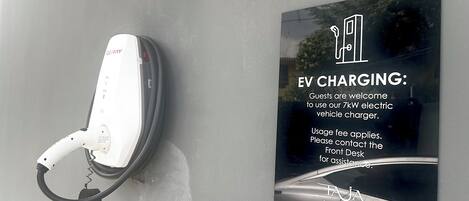 Un cargador para vehículo eléctrico y un cartel que detalla la disponibilidad de carga para vehículos eléctricos y las tarifas de uso.
