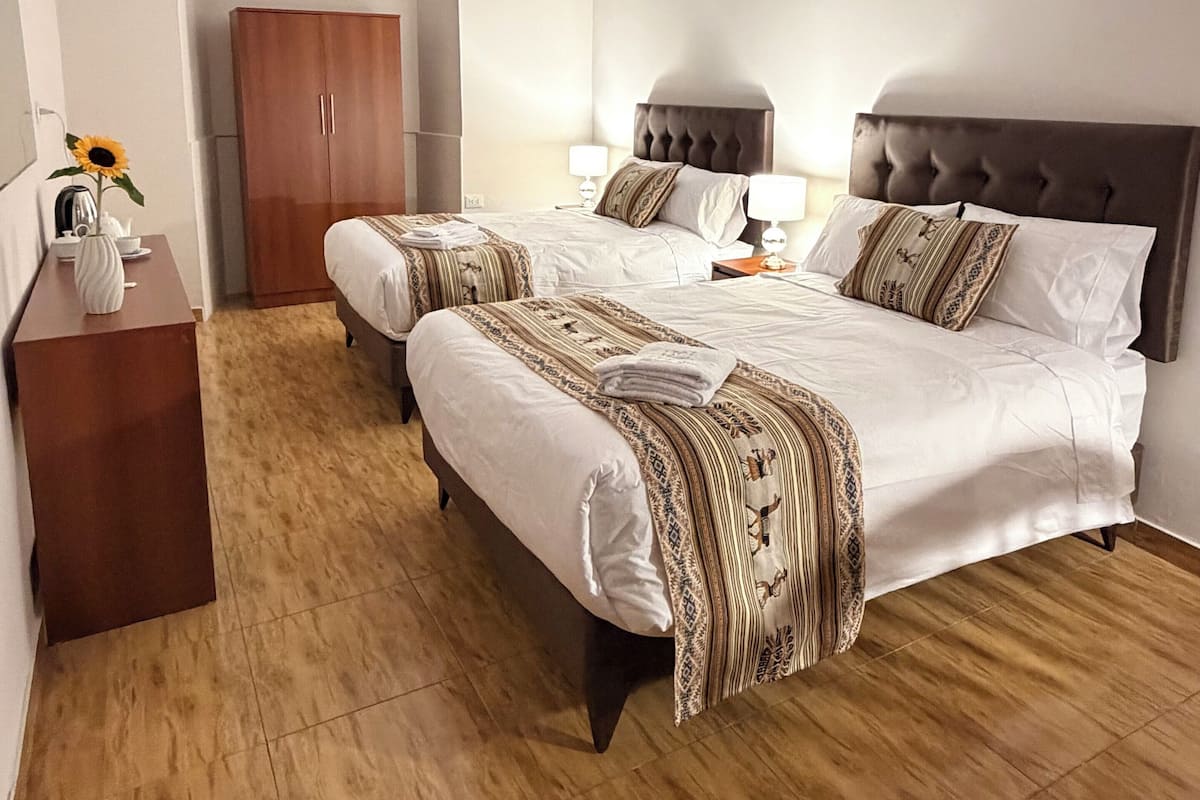Une chambre d’hôtel avec deux lits, une armoire en bois, un téléviseur à écran plat et un plancher en bois.