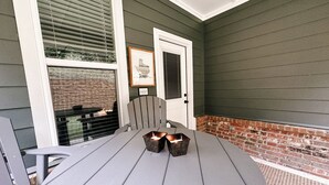 Eine überdachte Terrasse mit einem runden Tisch, zwei Stühlen und einem beleuchteten Kerzenarrangement.