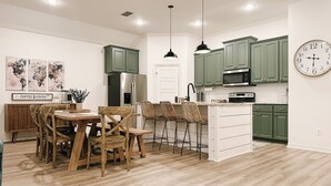 Eine moderne Küche mit grünen Schränken, einem Edelstahlkühlschrank, einer Mikrowelle und einem Essbereich mit Holztischen und einem Tisch.