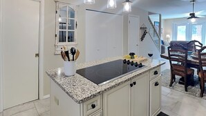 Une cuisine dotée d’un plan de travail en granit, de meubles blancs et d’une plaque de cuisson à induction noire.