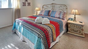 Une chambre avec un grand lit, deux tables de chevet avec des lampes, une fenêtre avec des rideaux et des œuvres d’art murales.