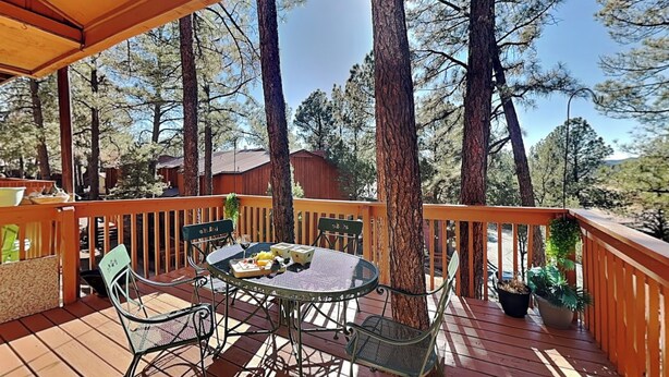 Une terrasse en bois avec une table ronde et des chaises, entourée d’arbres.