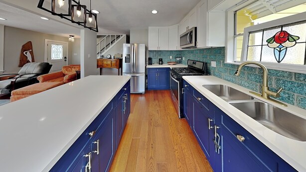 A modern kitchen with blue cabinets, a white countertop, a stainless steel sink, and a large island. - Yellow Belle on Avenue L (Galveston)