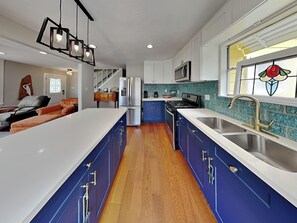 Eine moderne Küche mit blauen Schränken, einer weißen Arbeitsplatte, einer Edelstahl-Spüle und einer großen Kochinsel.