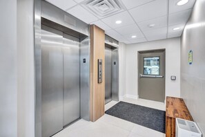 A modern elevator with a wooden panel, a door with a window, and a bench with a trash bin. - 2 Bedroom, 2 Bath Beach & Gulfside Condo (Sarasota)