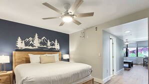 A bedroom with a bed, nightstands, a ceiling fan, a wall with a mountain design, and a view through an open door. - NEW LISTING|  Crested Butte Ski Suite, Pool & Hot Tub (Crested Butte)
