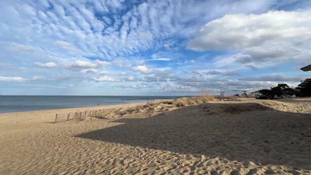 Una spiaggia con una recinzione di legno e dune.