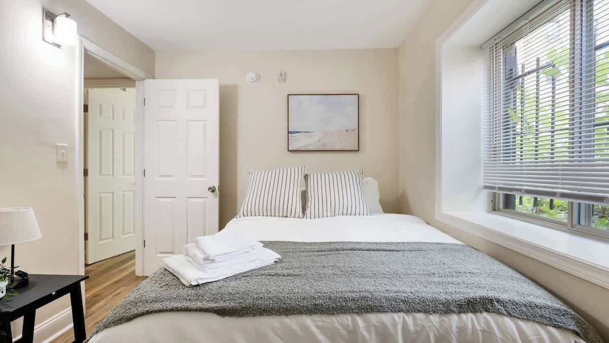 Een slaapkamer met een bed, een raam met zonwering, een deur en een aan de muur hangend schilderij.