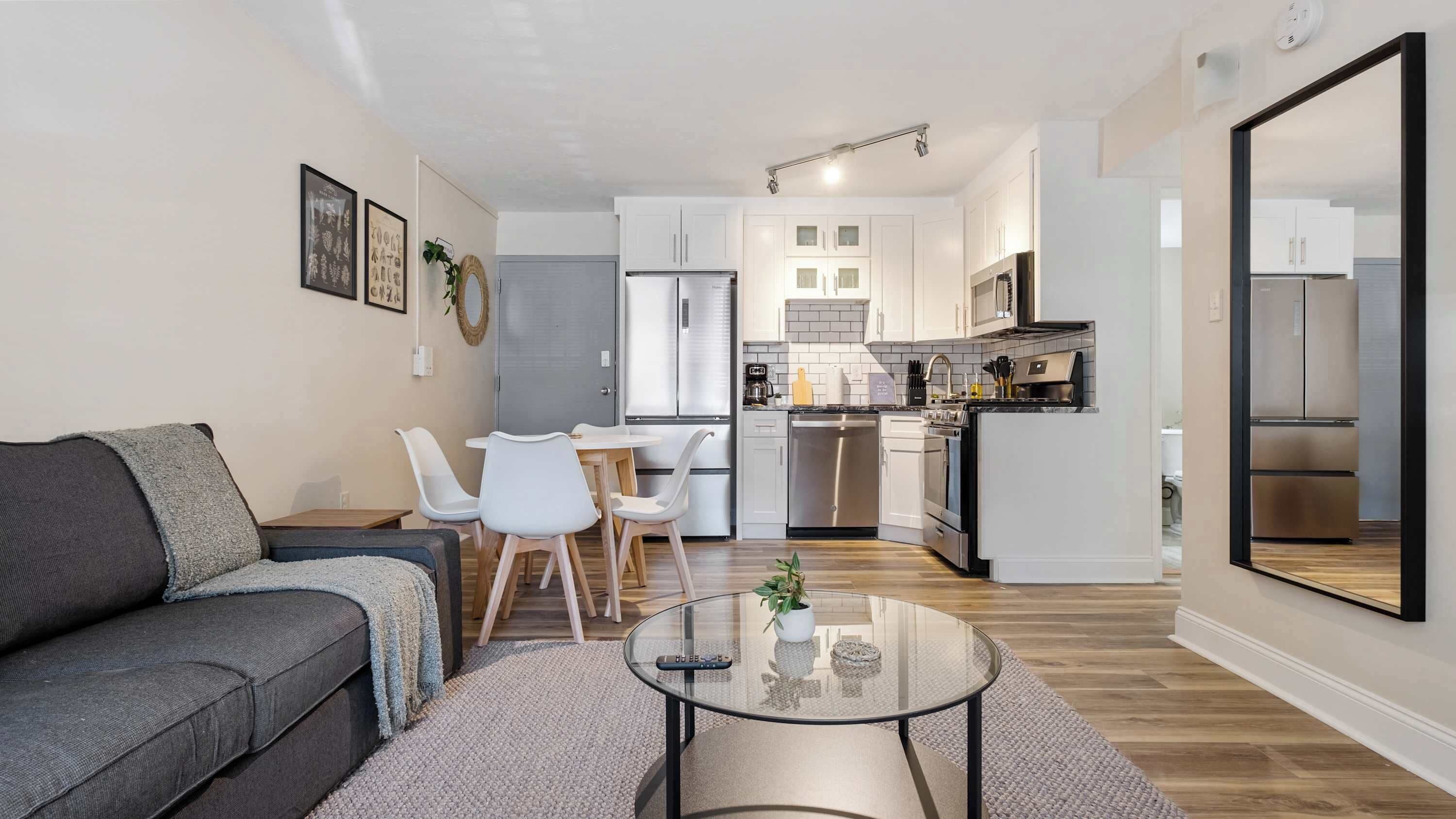 Un salon moderne avec un canapé gris, une table basse en verre et un coin repas avec des chaises blanches.
