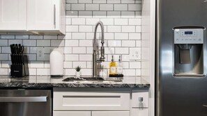 Une cuisine moderne avec des armoires blanches, un évier en acier inoxydable, un distributeur d’eau et un égouttoir à vaisselle.