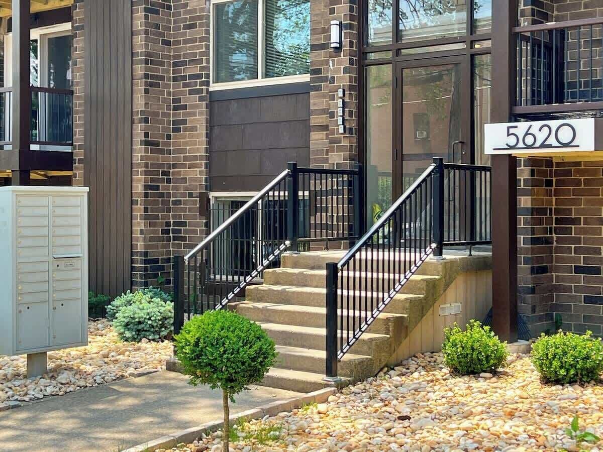A two-story building with a brick facade, a black metal staircase, and a mailbox with the number 5620.