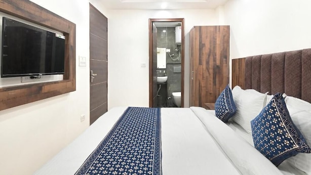 Un dormitorio con cama, televisor montado en la pared, armario y baño visible a través de una puerta abierta.