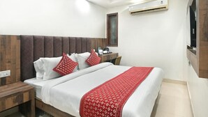 Un dormitorio con cama, mesita de noche, escritorio, ventana y aire acondicionado.