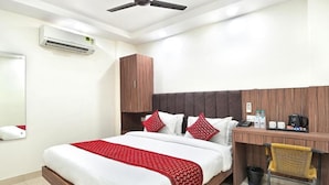 Una habitación de hotel con cama, escritorio, silla, ventilador de techo, aire acondicionado y un armario de madera.