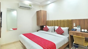 Habitación de hotel con cama, escritorio, silla, ventilador de techo, aire acondicionado y espejo.