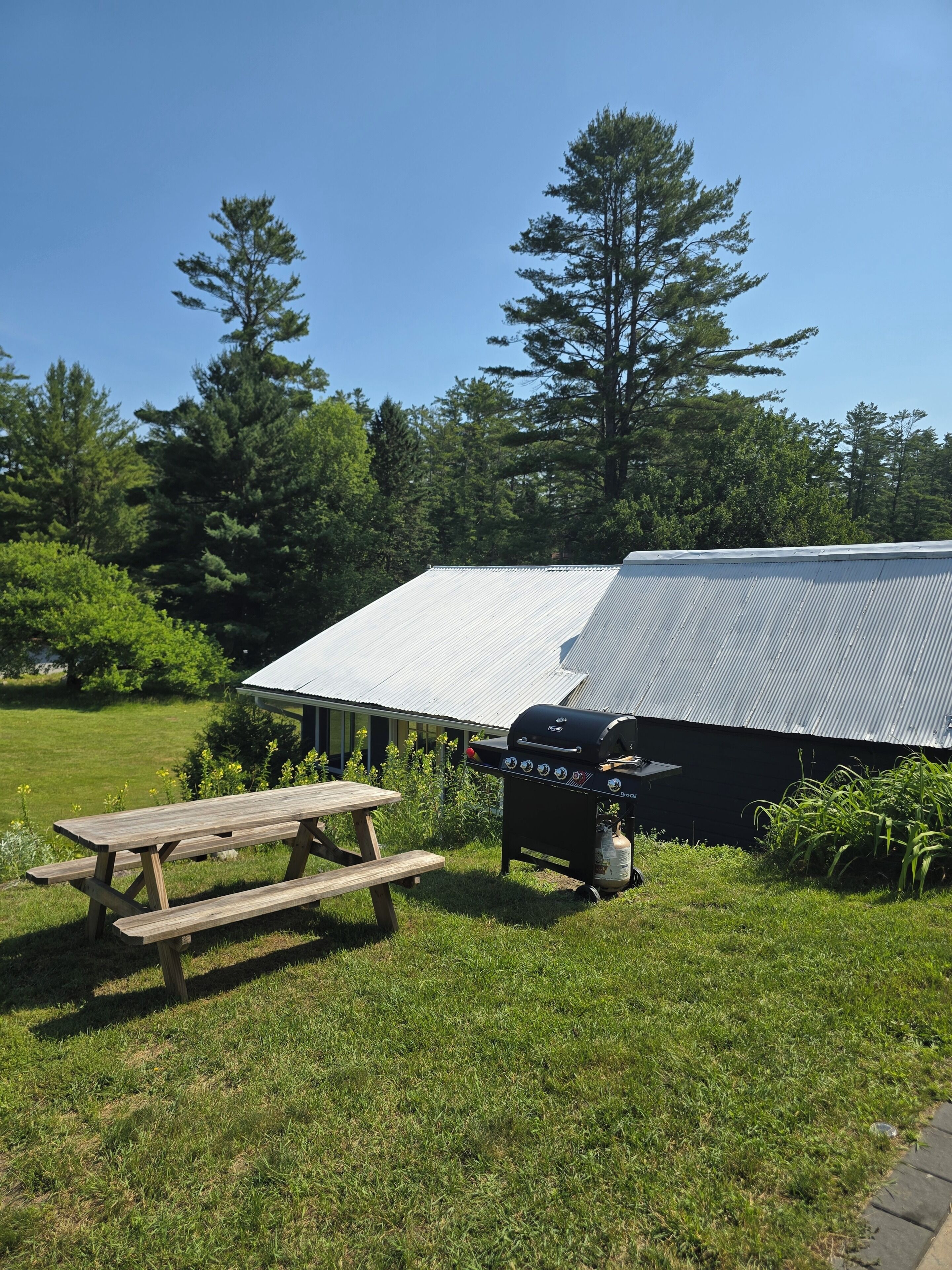 A picnic table and a barbecue grill in a grassy area with a building in the background.