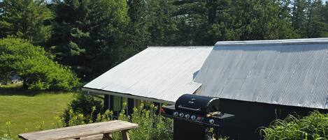 A picnic table and a barbecue grill in a grassy area with a building in the background.