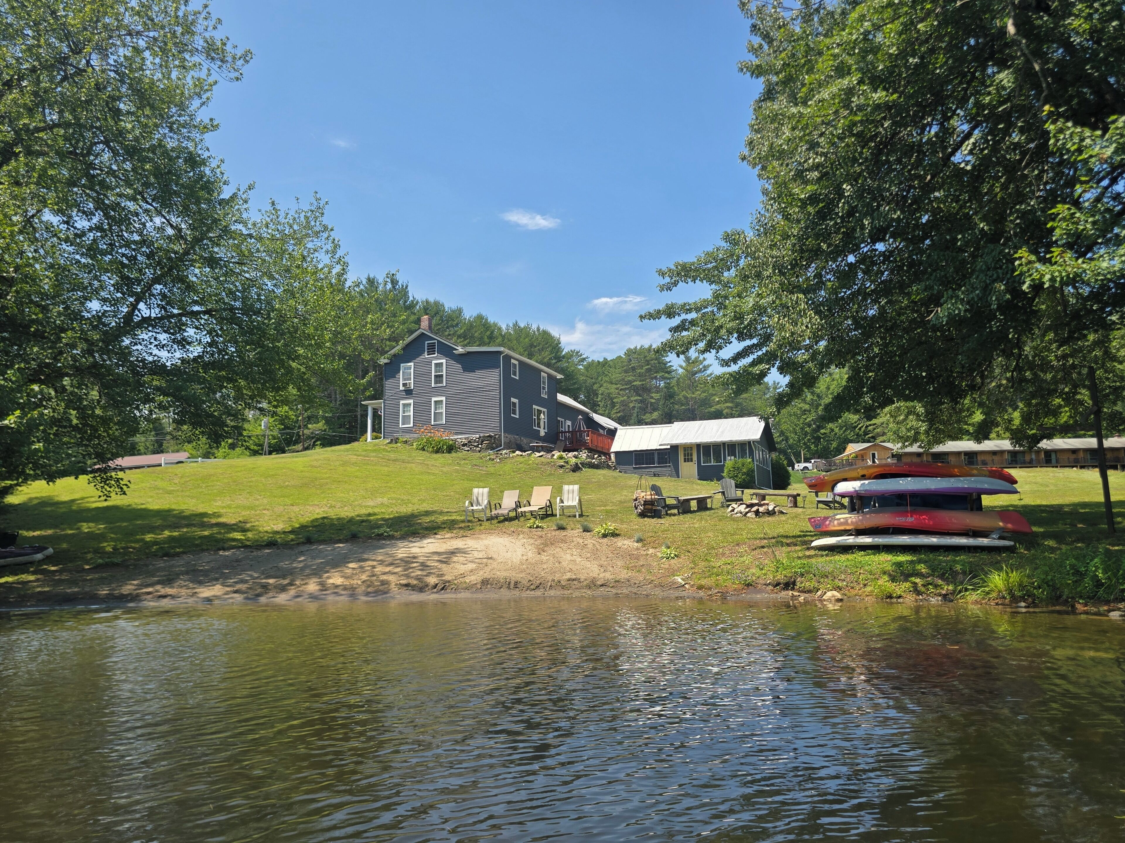 En fastighet vid en sjö med ett stort hus, utomhusmöbler och kanoter.