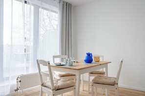 A dining area with a wooden table, white chairs, and a blue pitcher. - Apartment EDEN - 1 Min HBF - Ideal for trips to Cologne, Düsseldorf, Wuppertal (Solingen)