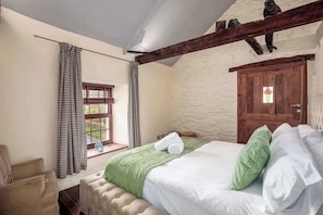 A bedroom with a bed, a window with curtains, a wooden door, and a stone wall.
