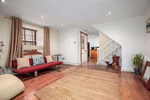 A spacious living area with a red sofa, a large woven rug, and a staircase leading to a kitchen.