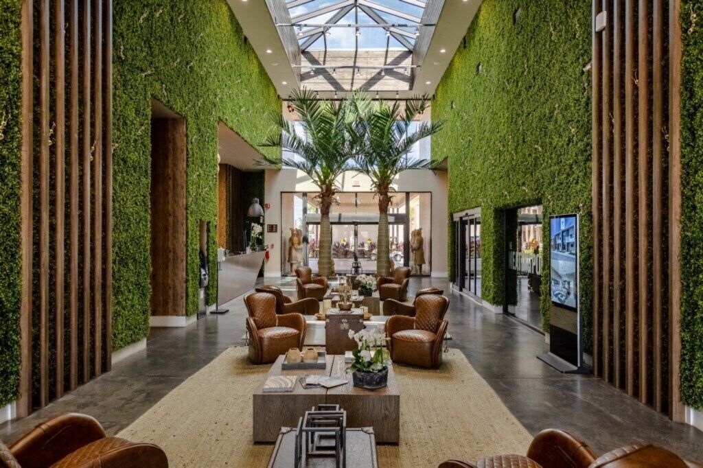 Un hall espacioso con techo alto, detalles de pared verde y un área de descanso central.