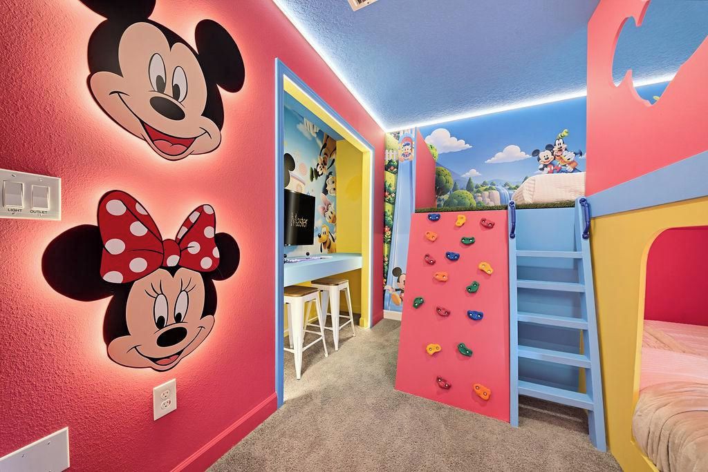 A child's room with Mickey and Minnie Mouse wall decals, a climbing wall, and a desk with a computer.