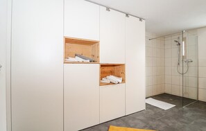 Moderni kylpyhuone, jossa on suihkukaappi, puiset säilytystilat ja laatoitettu lattia.