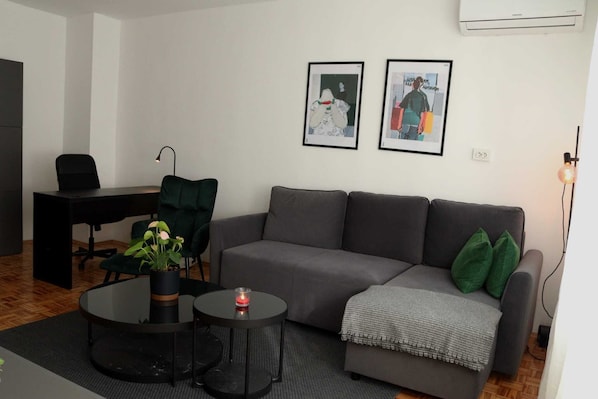 A modern living room with a grey sofa, a black desk, and two framed artworks on the wall.