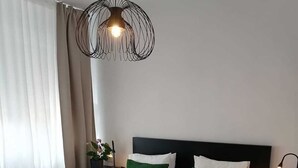 Un lit bien fait, avec une literie blanche et des coussins verts, un luminaire suspendu moderne et un plancher en bois.