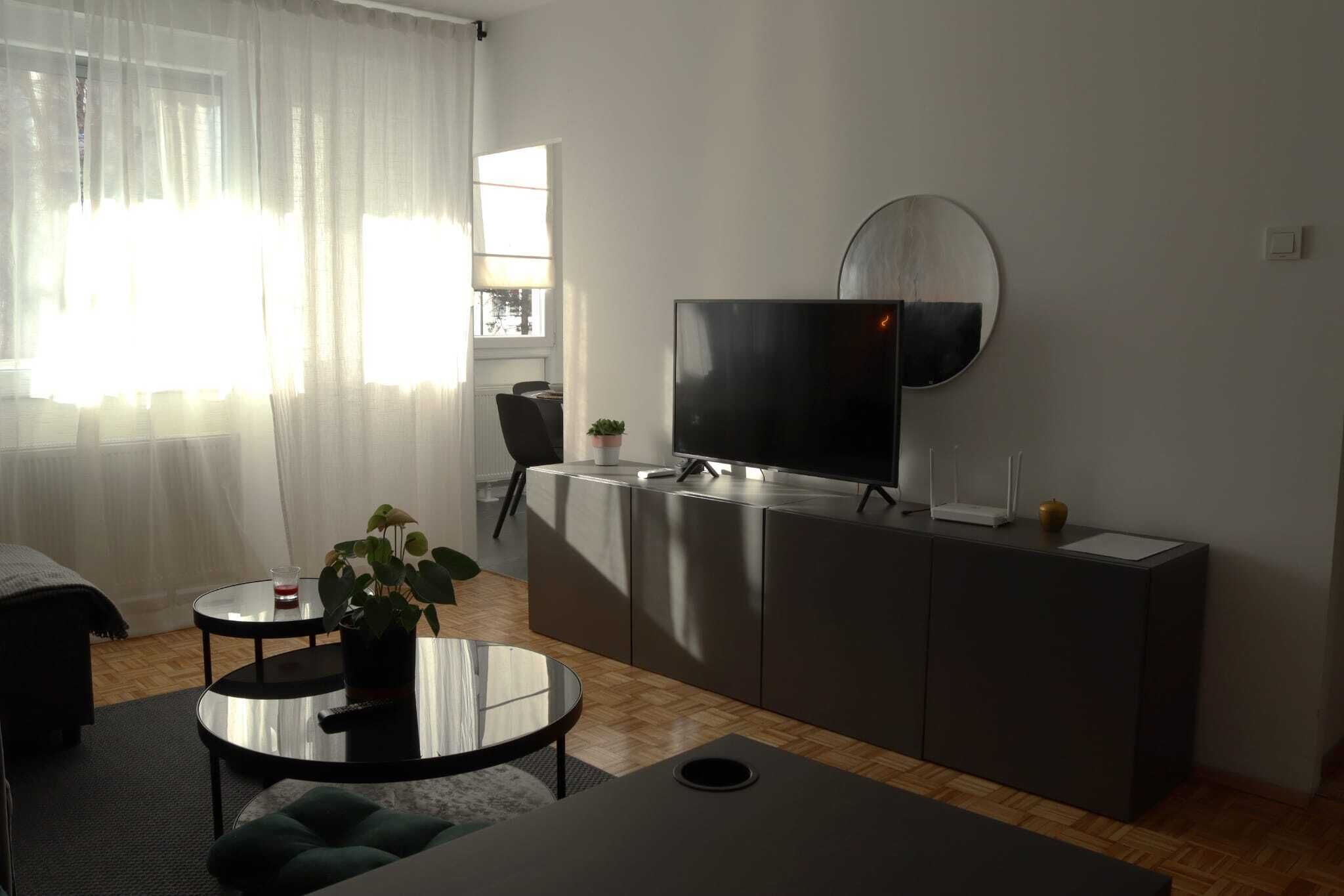 Un saló modern amb televisió de pantalla plana penjada a la paret, zona de dinar amb taula i cadires, i un espai d'estar acollidor amb un sofà i una taula baixa.