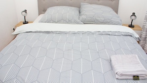 Un lit bien fait, recouvert d’une couvre-lit à motifs géométriques, avec deux oreillers, deux lampes de chevet et une serviette pliée posée sur le lit.