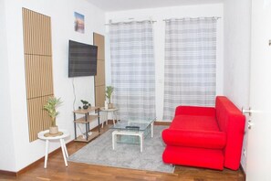 Una sala de estar moderna con un sofá rojo, una mesa de centro de vidrio, un televisor montado en la pared y un ventanal con cortinas a rayas.
