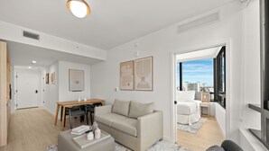 Una sala de estar moderna con sofá, reposapiés y comedor. Hay un ventanal con vista a la ciudad.