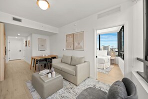 A modern living room with a sofa, ottoman, and dining area. There is a large window with a view of the city. - New Miami Downtown 2 BD / 2 BA City Skyline Views (Miami)