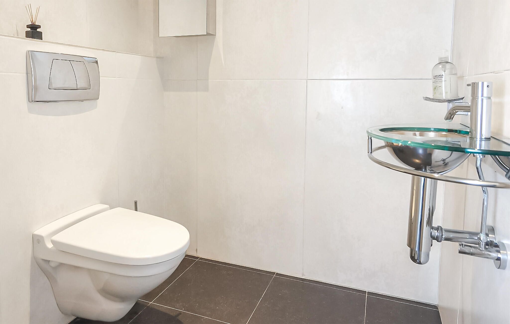 A bathroom with a white toilet, a glass sink with a chrome faucet, and a wall-mounted soap dispenser.
