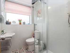 Ein Badezimmer mit Toilette, Waschbecken und Dusche. Es gibt ein Fenster mit rosa Jalousie, einen Spiegel und eine Vase mit Blumen.