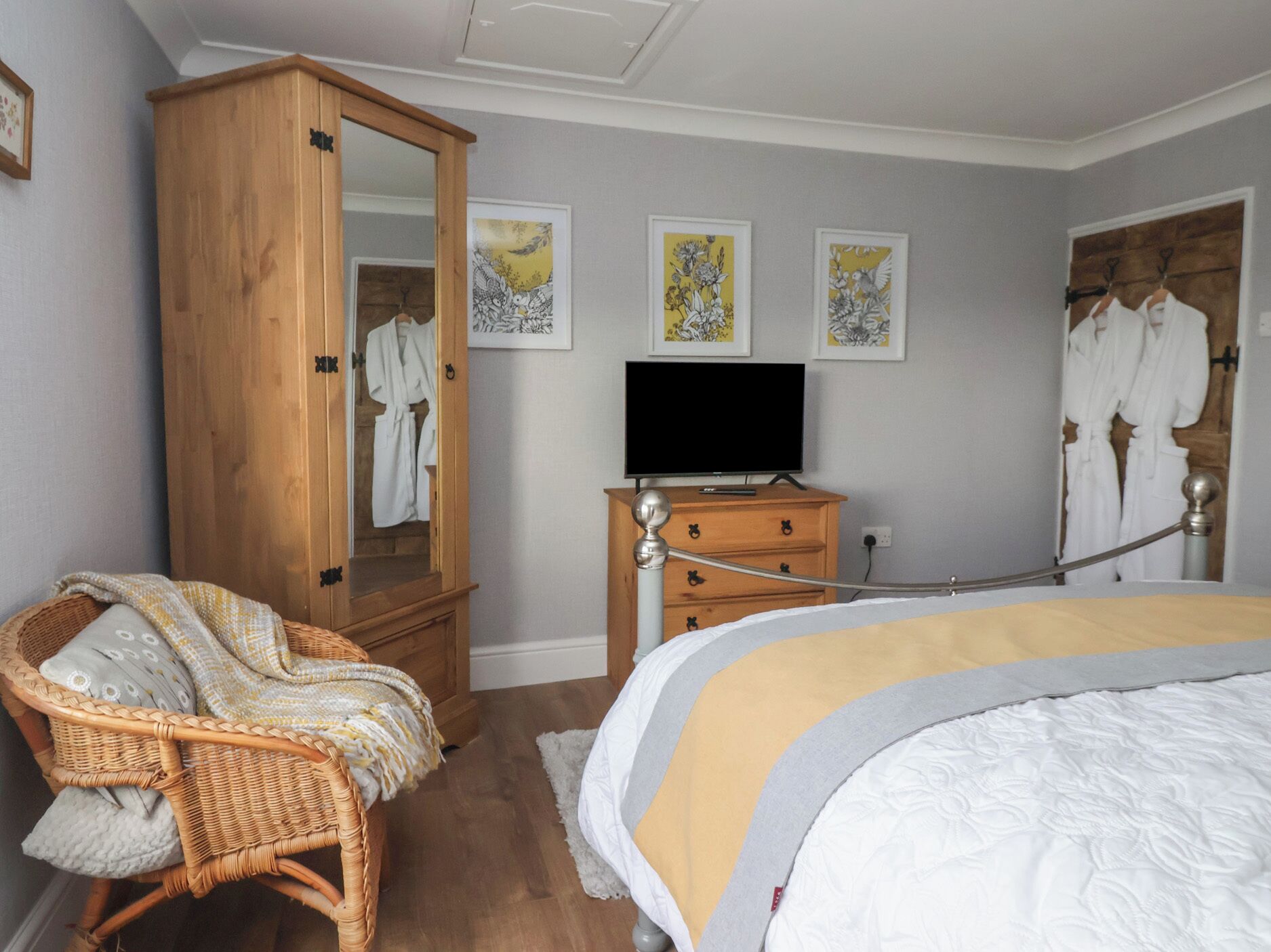 A bedroom with a wooden wardrobe, a television on a dresser, a wicker chair, and artwork on the wall.