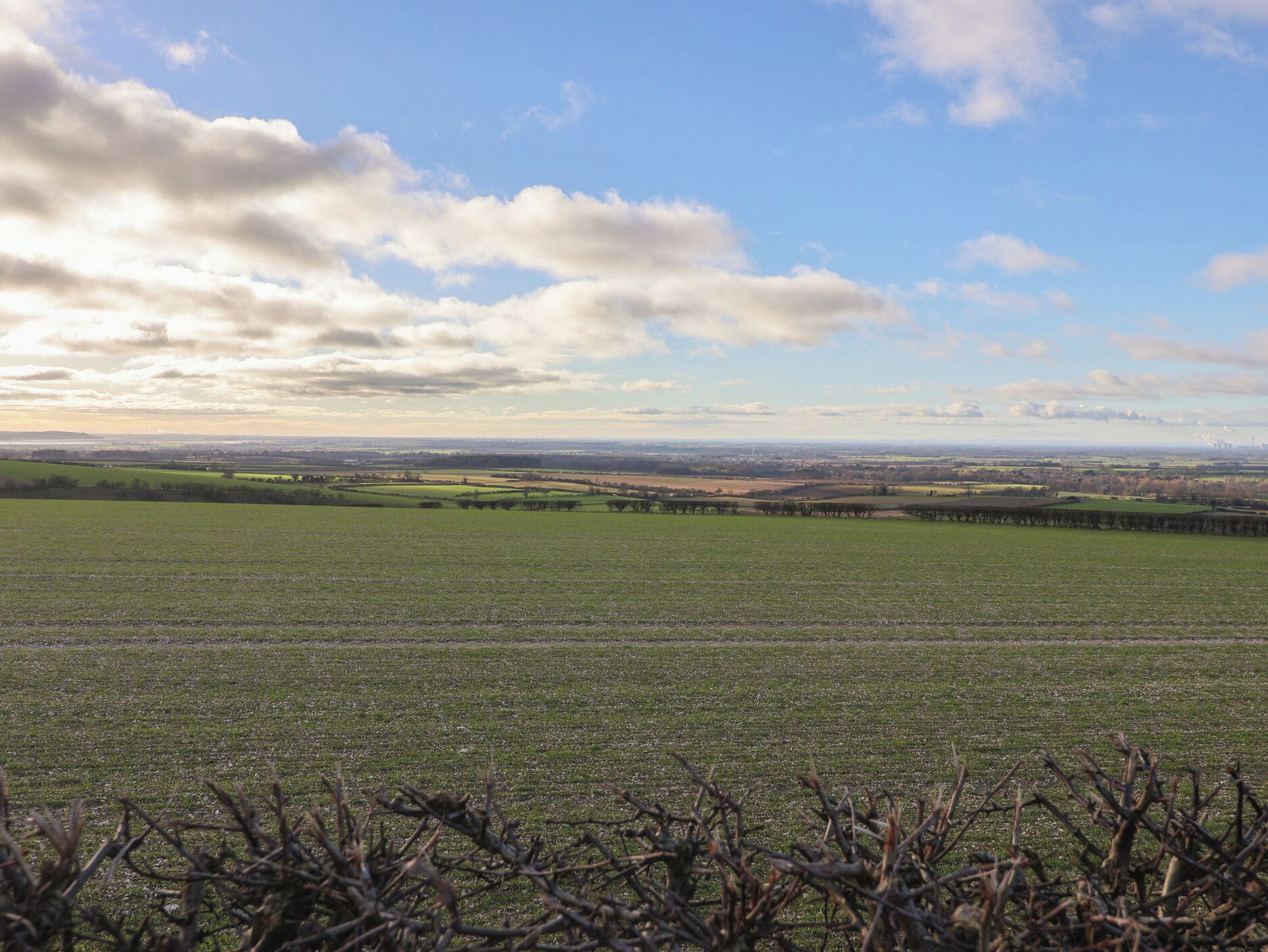 Eine weite, offene Landschaft mit weiter Aussicht auf eine Stadtlandschaft unter teils bewölktem Himmel.
