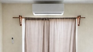 Ett sovrum med en säng, beige gardiner och en luftkonditioneringsanläggning.