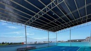 Un court de tennis extérieur, doté d’un filet, entouré d’une clôture métallique et couvert d’un toit.