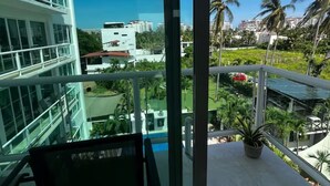 Un balcon donnant sur un immeuble moderne, un espace vert agrémenté de plantes et un ciel bleu dégagé.