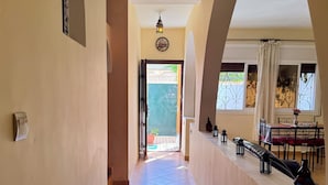 A hallway with a patterned rug, a clock, and a view of a dining area with a table and chairs. - Villa Riad Style (with garden access) - Wifi and Parking (Agadir)