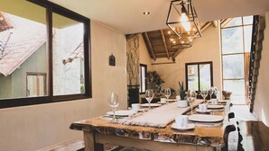 A dining area with a long wooden table set for a meal, large windows, and a stone wall. - Killay B1 - Gorgeous 3-bedroom villa in Calca perfect for your getaway (Calca)