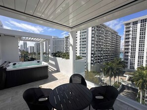 A balcony with a hot tub, two chairs, and a view of high-rise buildings. - South Beach Penthouse: Hot Tub + Rooftop Pool #501 (Miami Beach)