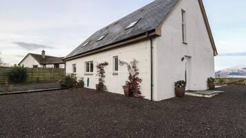 Une maison de plain-pied avec un toit en pente, des murs extérieurs blancs et une allée gravillonnée.