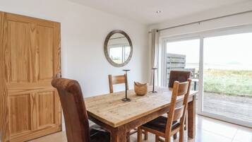 A dining area with a wooden table, four chairs, a round mirror, and a view through a glass door.