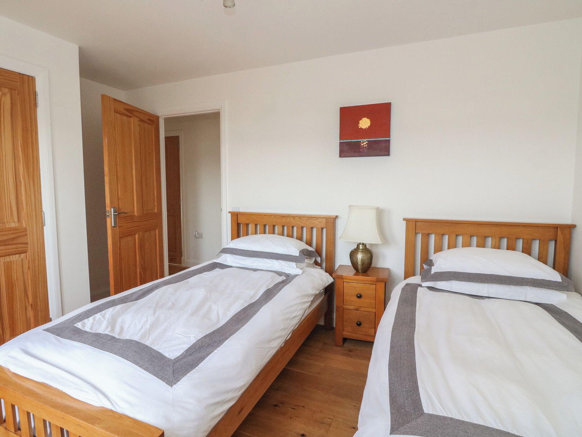 Une chambre à coucher avec deux lits en bois, une table de chevet avec une lampe et une porte donnant sur une autre pièce.